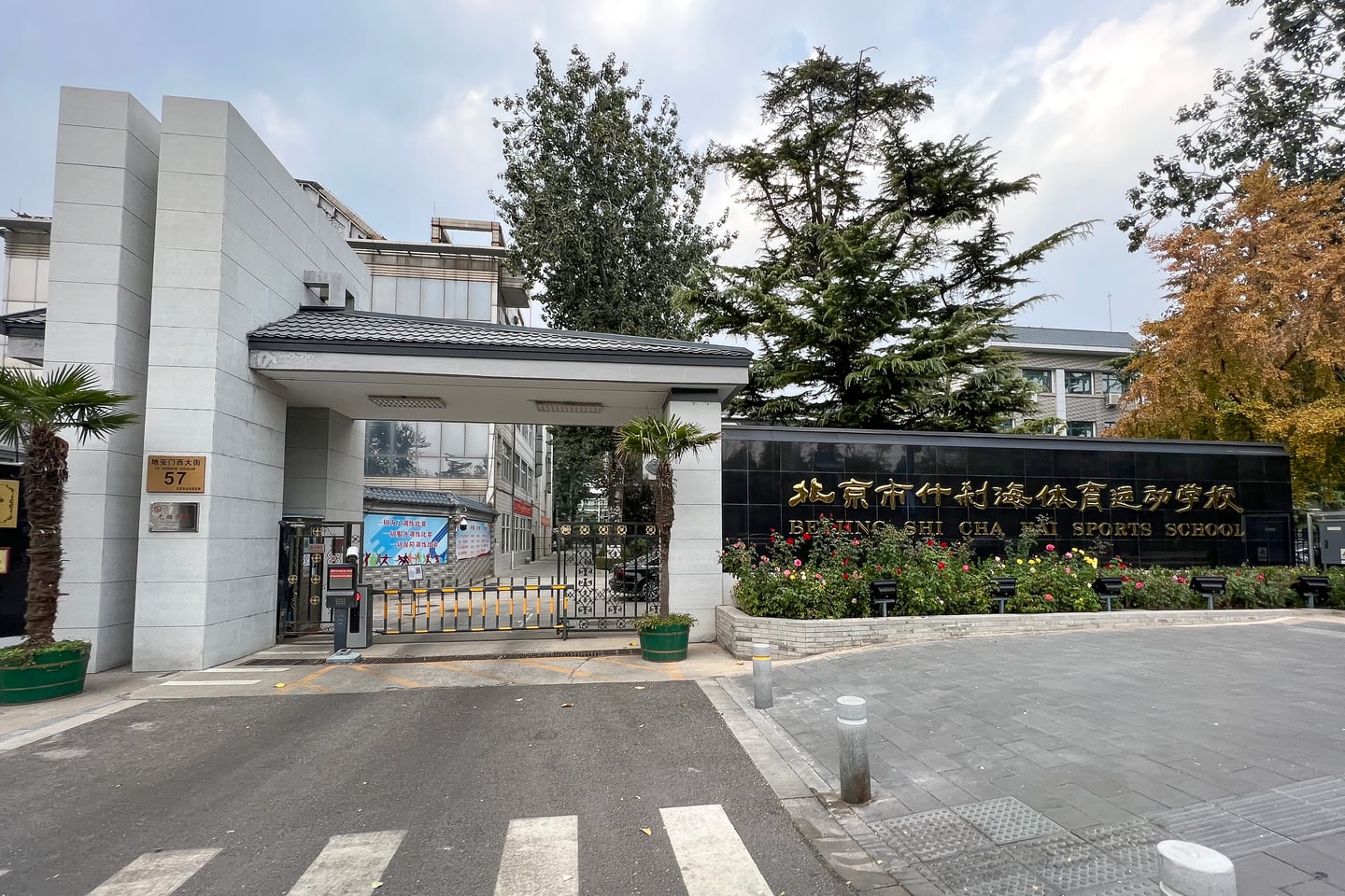 베이징 스차하이, 금색 글씨로 학교 이름이 새겨진 검은 대리석 벽과 현대적인 정문 건물이 조화를 이루는 스차하이 스포츠 학교의 입구 모습입니다.