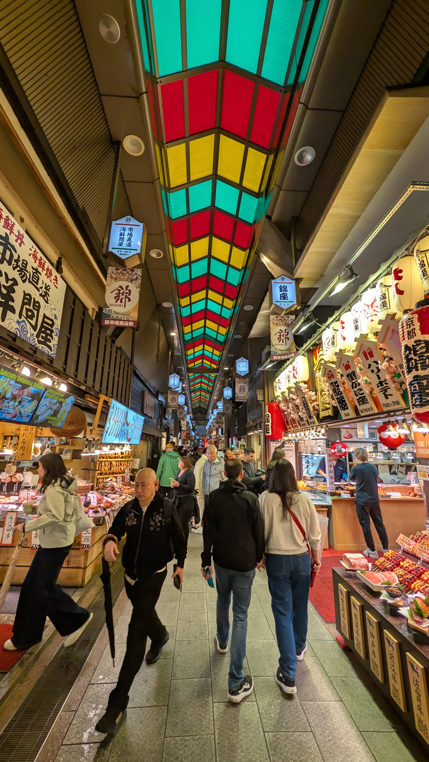 교토 니시키 시장, 화려한 색상의 아케이드 천장 아래로 활기 넘치는 상점가와 인파가 어우러진 풍경입니다.
