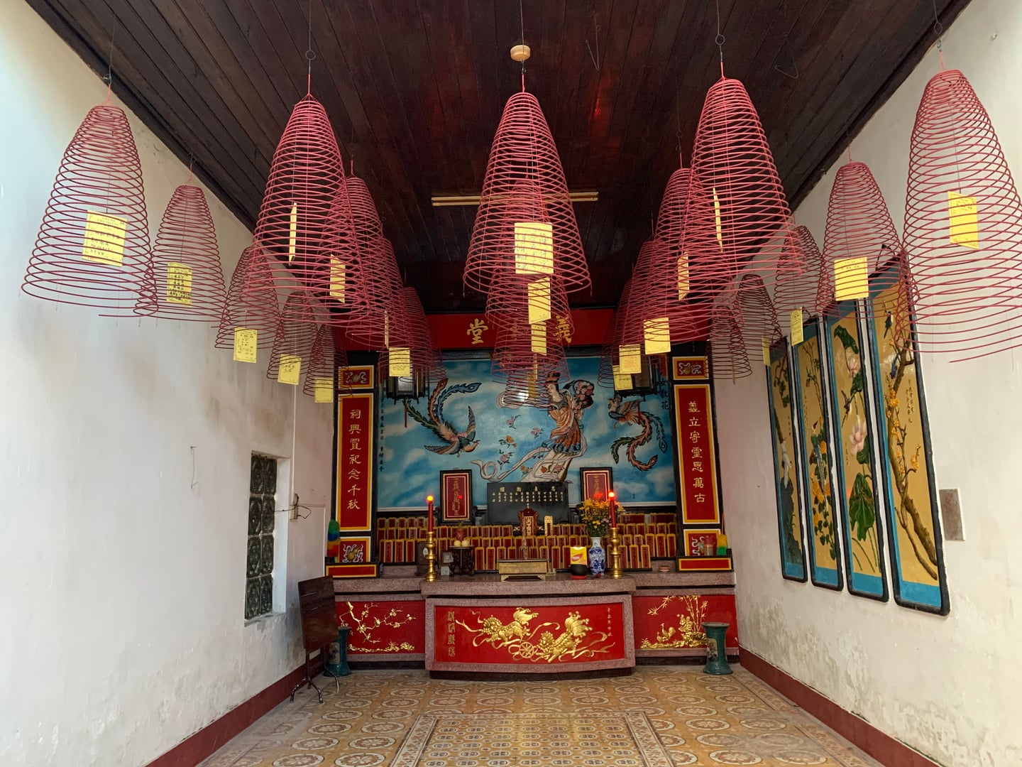 호이안 광조회관, 천장에 매달린 붉은 나선형 향들과 화려한 금색 장식의 제단이 어우러진 신비로운 내부 전경입니다.