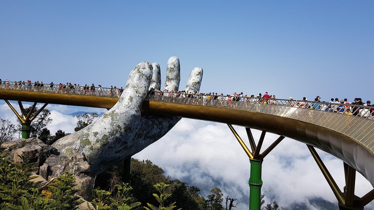 다낭 바나힐의 상징적인 명소인 골든 브릿지(Golden Bridge)의 모습입니다. 거대한 신의 손이 황금색 다리를 받치고 있는 독특한 디자인과 구름 위에 떠 있는 듯한 풍경이 잘 나타나 있습니다.