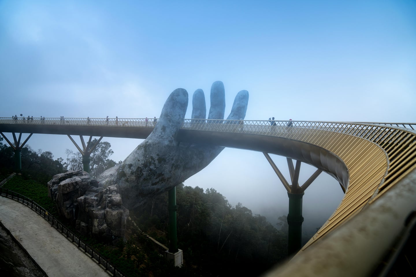 다낭 바나힐의 상징적인 명소인 골든 브릿지(Golden Bridge)의 모습입니다. 거대한 신의 손이 황금색 보행교를 받치고 있는 독특한 디자인이 안개 낀 산의 풍경과 어우러져 신비로운 분위기를 자아냅니다.