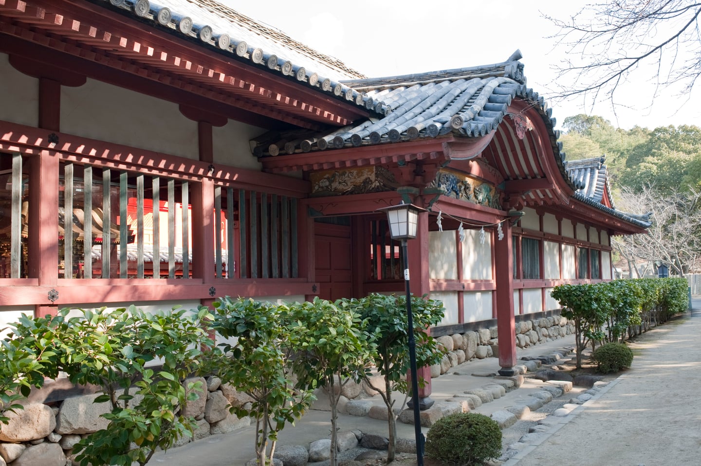 마쓰야마 이사니와 신사, 붉은 목조 기둥과 전통 기와가 어우러진 신사 건물의 측면 외관과 정돈된 정원 풍경입니다.