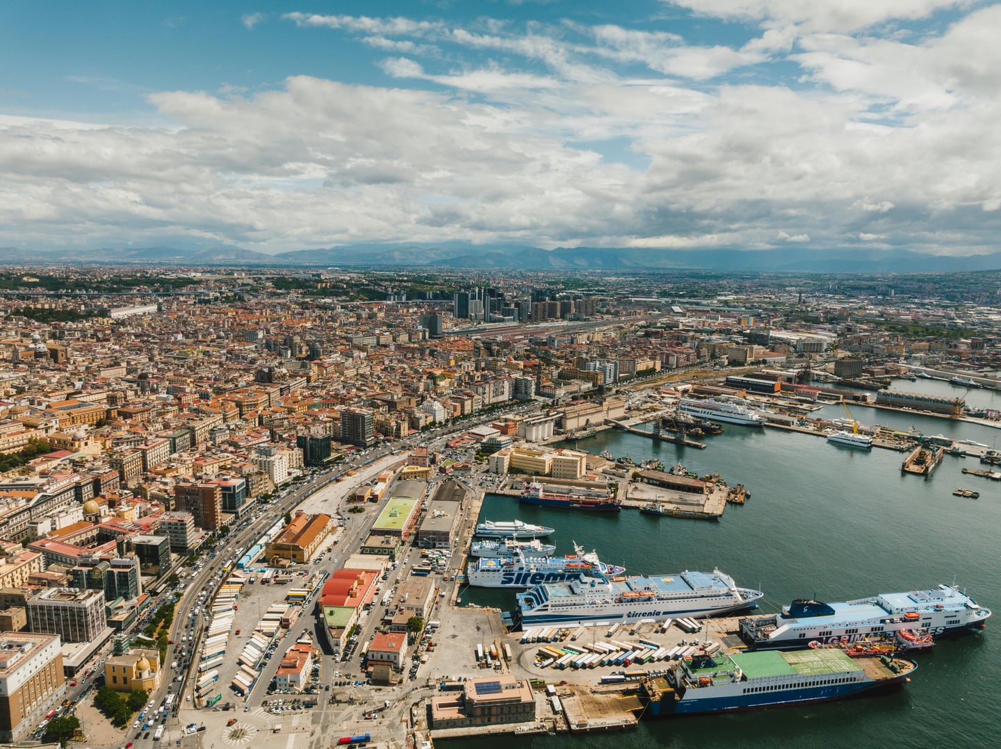 나폴리 나폴리 항구, 푸른 바다 위에 정박한 대형 페리들과 해안선을 따라 펼쳐진 고풍스러운 도시 전경이 인상적입니다.