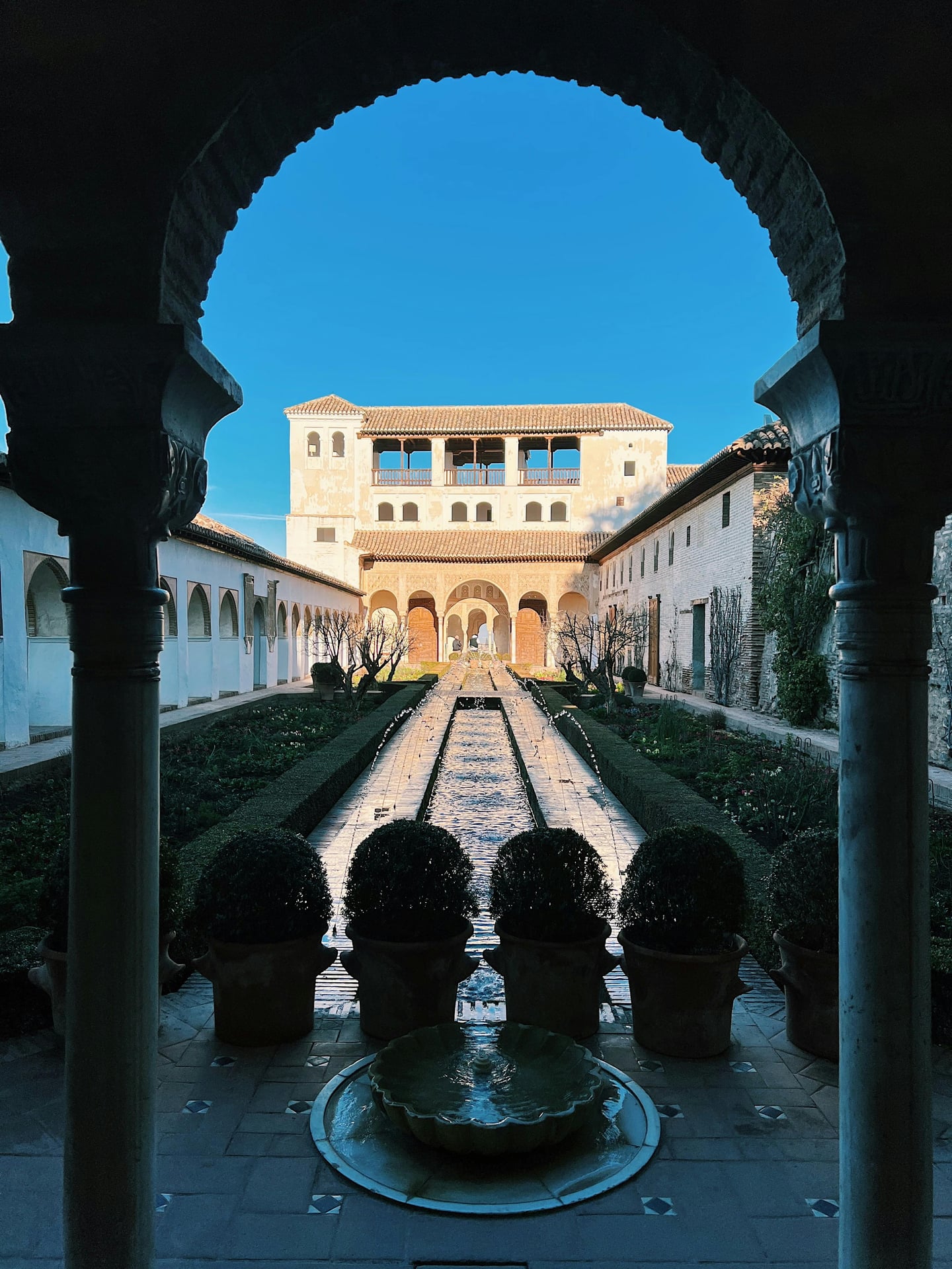 그라나다 헤네랄리페 정원, 아치형 기둥 너머로 보이는 긴 수로와 분수가 어우러진 이슬람 양식의 아름다운 중정 풍경입니다.