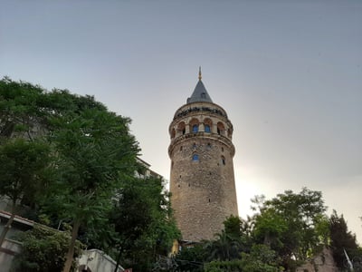이스탄불 갈라타 타워, 푸른 나무들 사이로 우뚝 솟은 고풍스러운 석조 타워와 원뿔형 지붕이 맑은 하늘 아래 펼쳐진 풍경입니다.