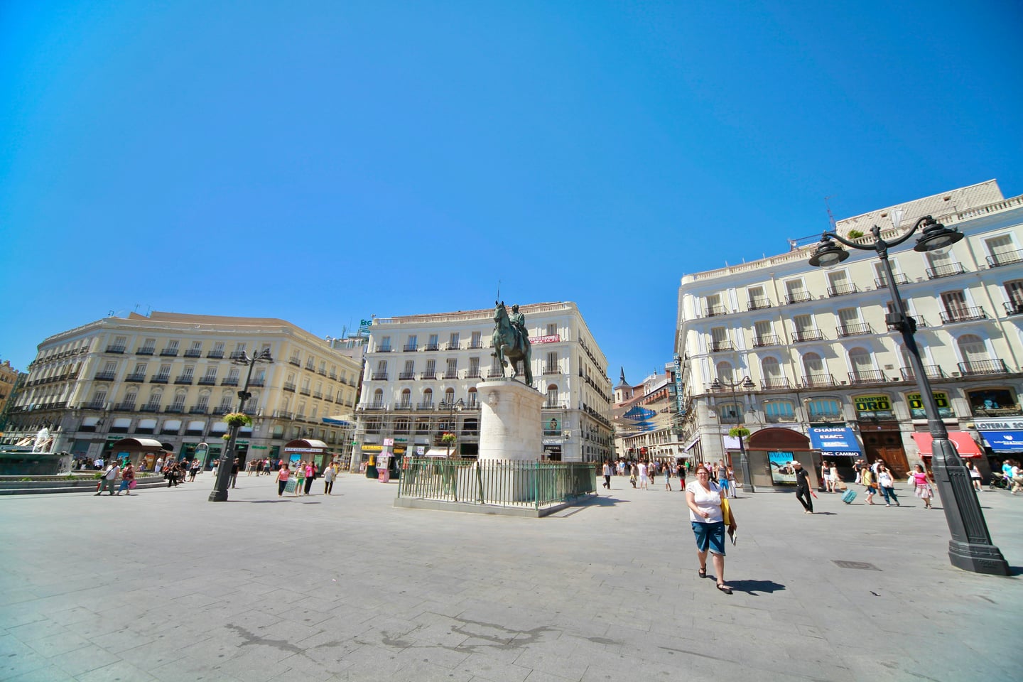 마드리드 푸에르타 델 솔, 푸른 하늘 아래 카를로스 3세 기마상과 고전적인 건축물들이 어우러진 광장의 활기찬 낮 풍경입니다.