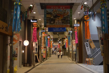마쓰야마 도고 상점가, 화려한 타나바타 장식과 도고 리본 현수막이 걸린 아케이드 거리를 산책하는 사람들의 모습입니다.