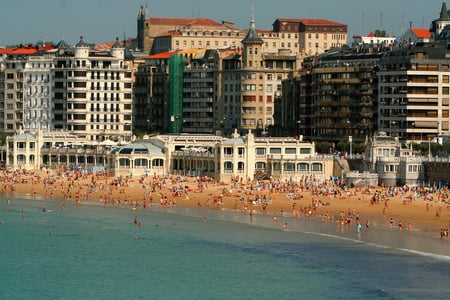 산세바스티안 라 콘차 해변, 고풍스러운 도심 건물들을 배경으로 황금빛 백사장에서 해수욕을 즐기는 수많은 사람들의 활기찬 풍경입니다.