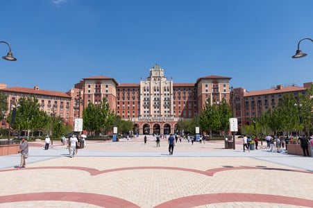 베이징 유니버셜 스튜디오, 맑은 푸른 하늘 아래 펼쳐진 화려한 대칭형 입구 호텔 건물과 활기찬 광장의 전경입니다.