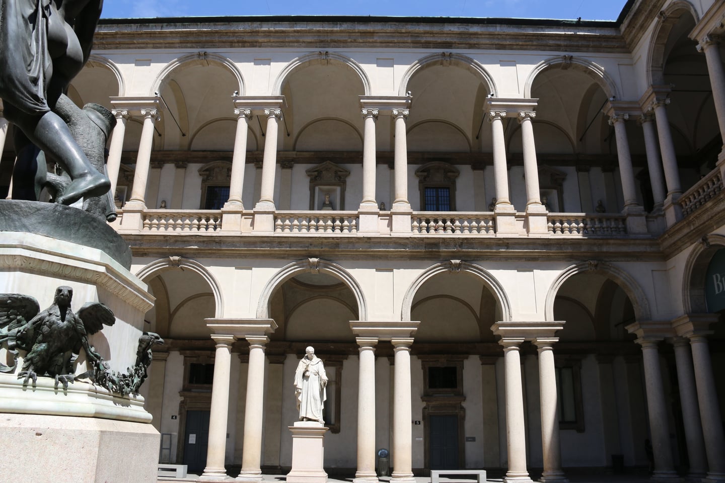 밀라노 브레라 미술관, 고전적인 아치형 회랑과 정교한 조각상이 어우러진 우아한 안뜰의 전경입니다.