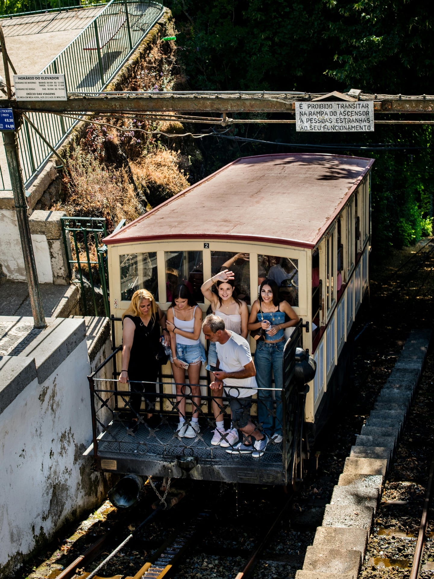 브라가 봉 제수스 푸니쿨라, 클래식한 목재 차량 데크에 탑승하여 손을 흔들며 즐거워하는 관광객들의 활기찬 모습입니다.