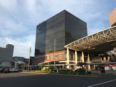 가고시마 가고시마 중앙역, 세련된 검은색 유리 외벽의 역사 건물과 탁 트인 광장이 어우러진 맑은 날의 풍경입니다.