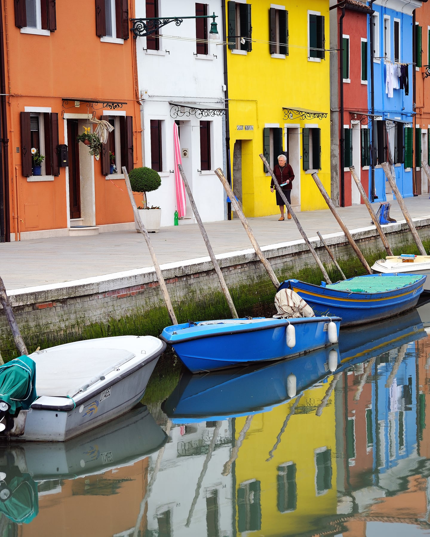 베니스 부라노섬, 운하를 따라 늘어선 알록달록한 원색 건물들과 수면에 반사된 화려한 색채가 어우러진 평화로운 마을 풍경입니다.