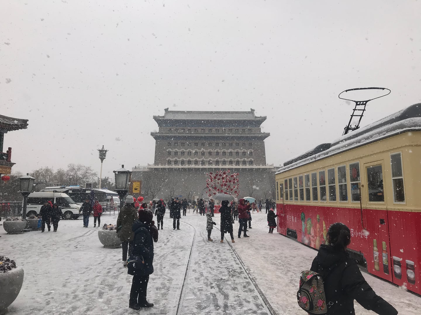 베이징 전문대가, 눈 덮인 거리 위로 웅장한 정양문 화살루와 붉은색 관광 전차가 어우러진 겨울 풍경입니다.