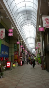 가고시마 가고시마 노면전차, 화사한 꽃과 잔디가 깔린 궤도 옆으로 노란색 전차가 정차해 있는 평화로운 도심 풍경입니다.