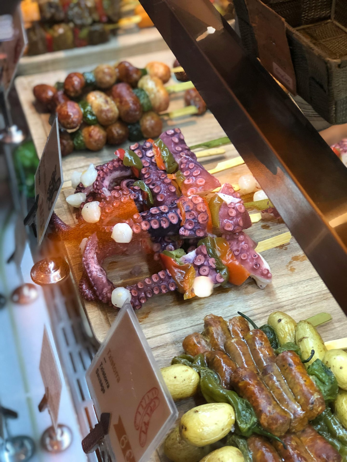 마드리드 타파스, 신선한 문어 다리와 노릇하게 구워진 소시지 꼬치가 시장 진열대 위에 먹음직스럽게 놓여 있는 모습입니다.