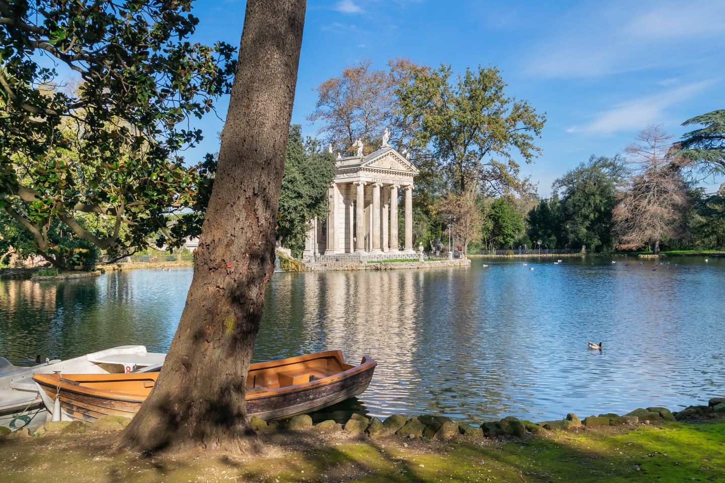 로마 빌라 보르게세 공원, 잔잔한 호수 위에 비치는 아스클레피오스 신전의 고전적인 기둥과 평화로운 숲의 전경이 어우러진 모습입니다.