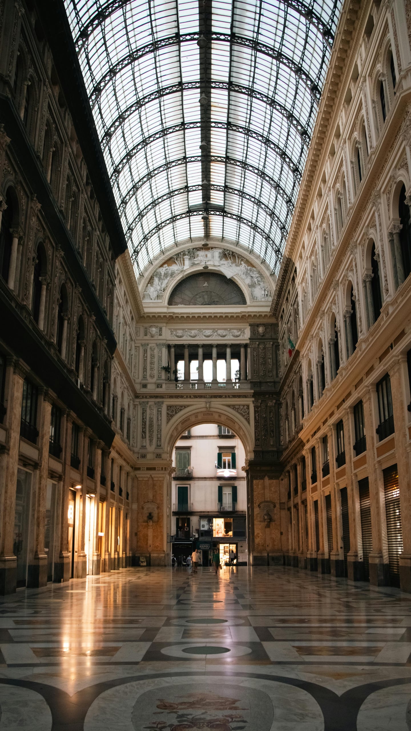 나폴리 움베르토 1세 갤러리, 웅장한 유리 천장 아래로 펼쳐진 화려한 대리석 바닥과 고전적인 아치형 건축 양식이 돋보이는 내부 전경입니다.