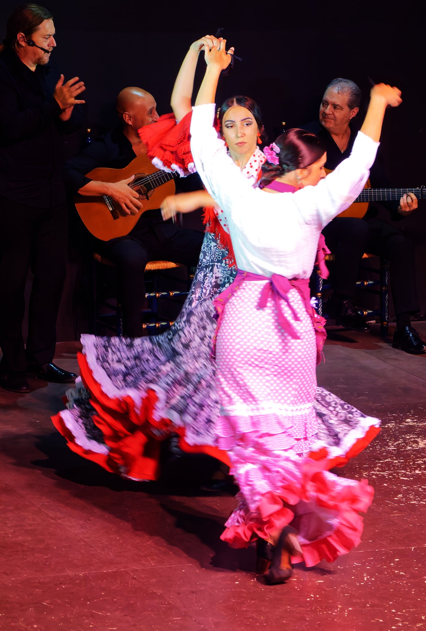 세비야 플라멩고 쇼, 화려한 붉은색과 흰색 드레스를 입은 무용수들이 기타 연주에 맞춰 역동적인 춤사위를 선보이는 열정적인 공연 현장입니다.