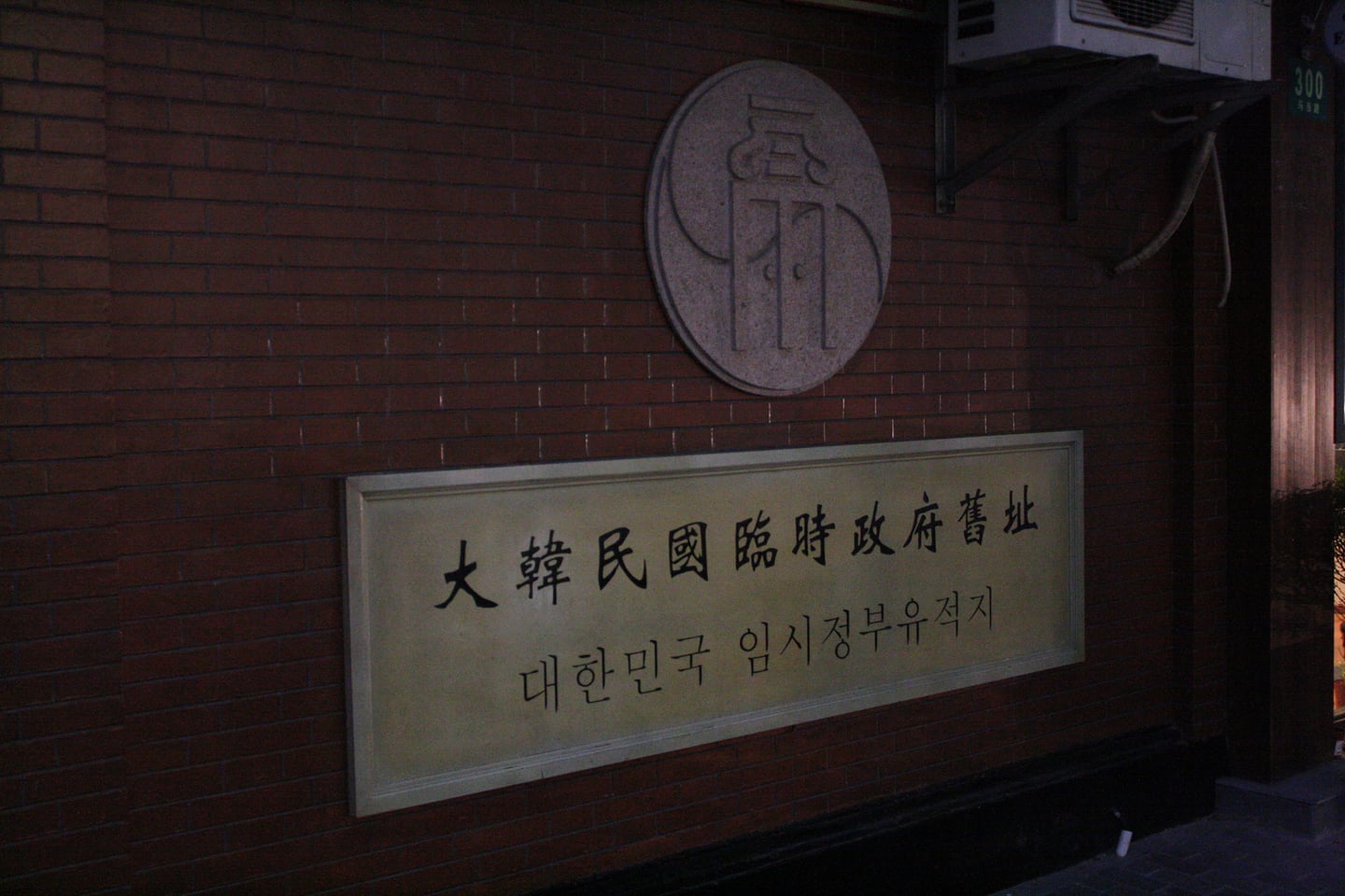 상하이 대한민국 임시정부청사, 붉은 벽돌 벽면에 한글과 한자로 정갈하게 새겨진 유적지 현판과 원형 상징 문양이 역사적인 분위기를 자아냅니다.