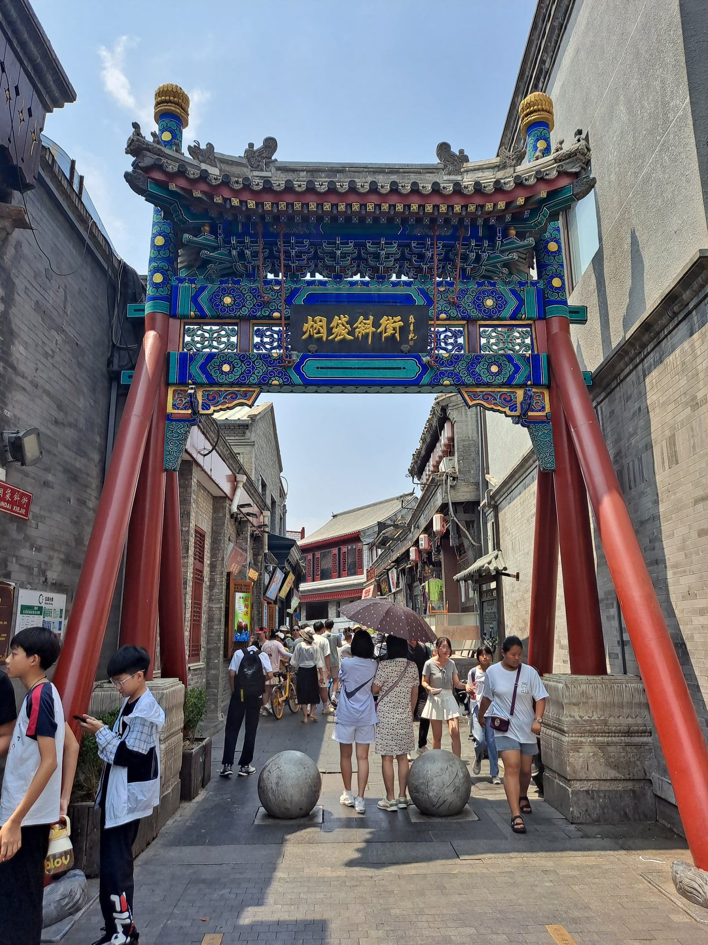 베이징 연대사 거리, 화려한 문양의 전통 패루 아래로 활기차게 오가는 관광객들과 고풍스러운 후통 골목의 풍경입니다.