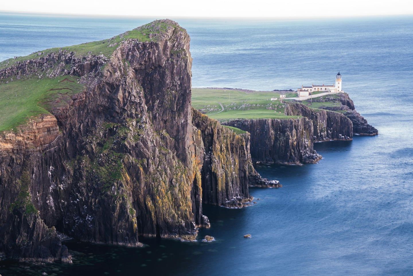 스카이 섬 네이스트 포인트, 푸른 바다를 향해 뻗어 나간 거대한 해안 절벽 끝에 우뚝 솟은 하얀 등대의 이국적인 풍경입니다.