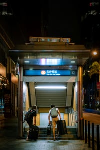 홍콩 침사추이, 밤거리의 환한 조명 아래 커다란 캐리어를 들고 침사추이 지하철역 입구로 들어가는 여행객들의 뒷모습입니다.