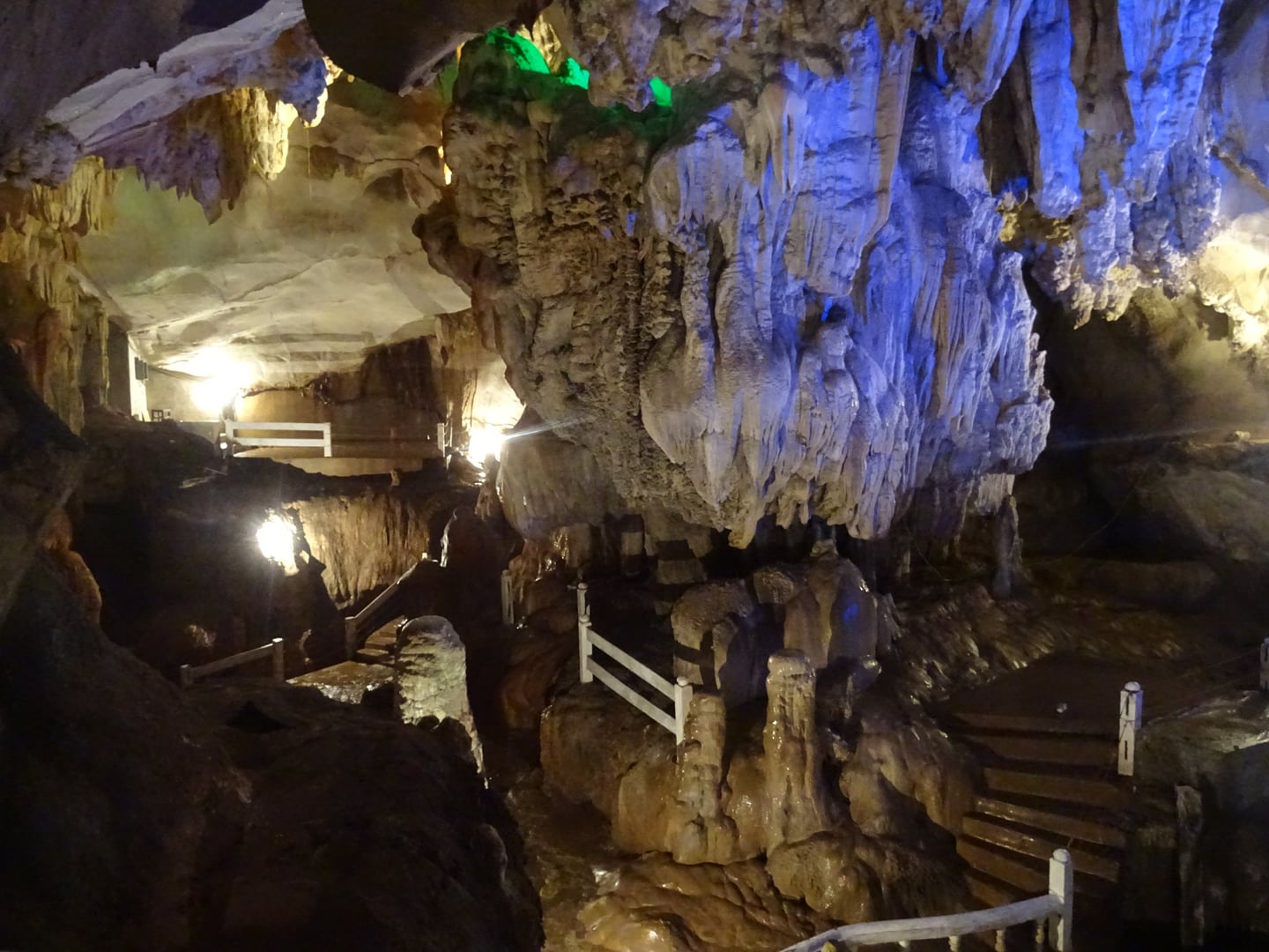 방비엥 탐짱 동굴, 푸른 조명이 비치는 거대한 종유석과 관람객을 위한 흰색 난간이 설치된 신비로운 동굴 내부 전경입니다.