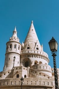 부다페스트 어부의 요새, 맑은 하늘 아래 우뚝 솟은 하얀 석조 탑과 고전적인 가로등이 어우러진 이국적인 풍경입니다.