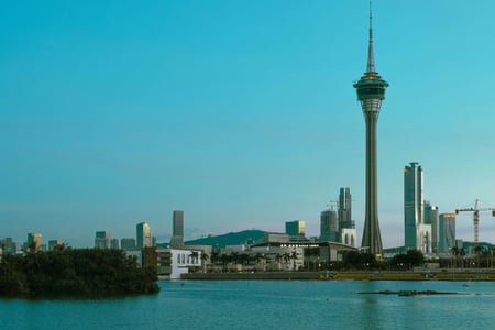 마카오 마카오 타워, 해질녘 푸른 하늘 아래 강물 너머로 우뚝 솟은 타워와 현대적인 도시 스카이라인이 어우러진 풍경입니다.