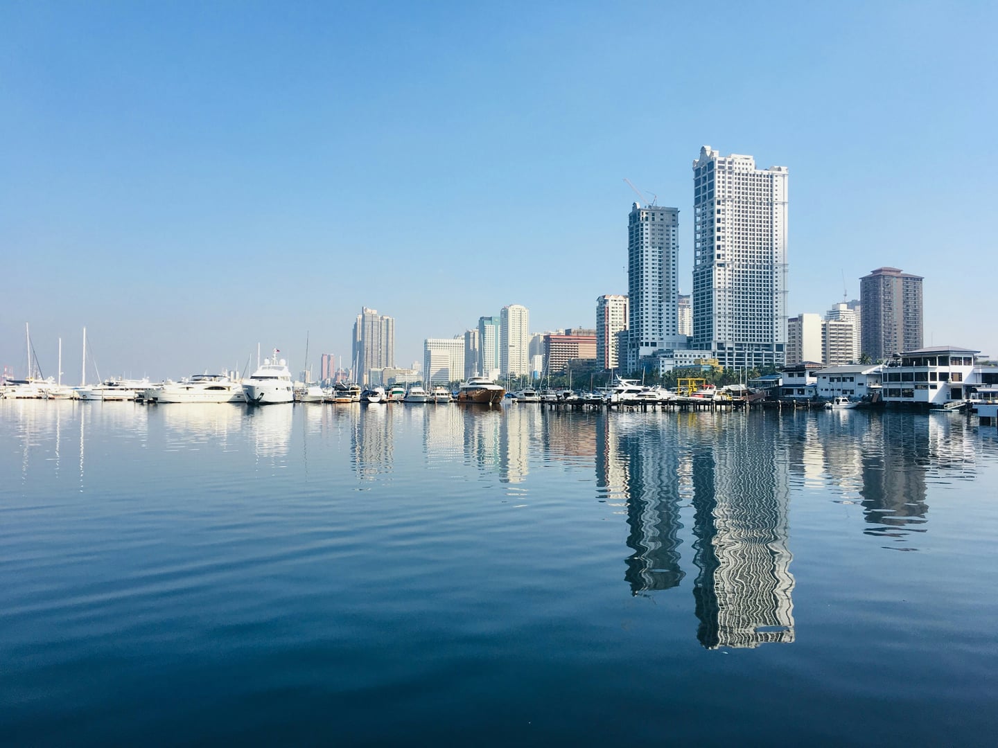 마닐라 마닐라 베이, 푸른 바다 위로 요트 선착장과 고층 빌딩들이 아름답게 반사되는 평온한 항구의 전경입니다.