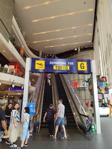 파타야 터미널 21, 공항 게이트를 연상시키는 도쿄행 안내판과 에스컬레이터를 이용하는 방문객들의 활기찬 쇼핑몰 내부 전경입니다.