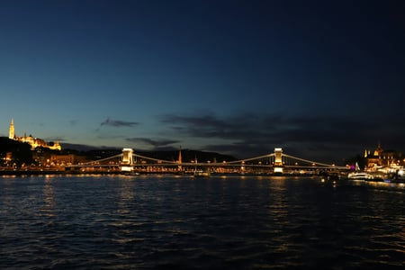 부다페스트 세체니 다리, 어스름한 밤하늘 아래 다뉴브 강을 가로지르며 화려한 황금빛 조명을 밝히고 있는 웅장한 현수교의 야경입니다.