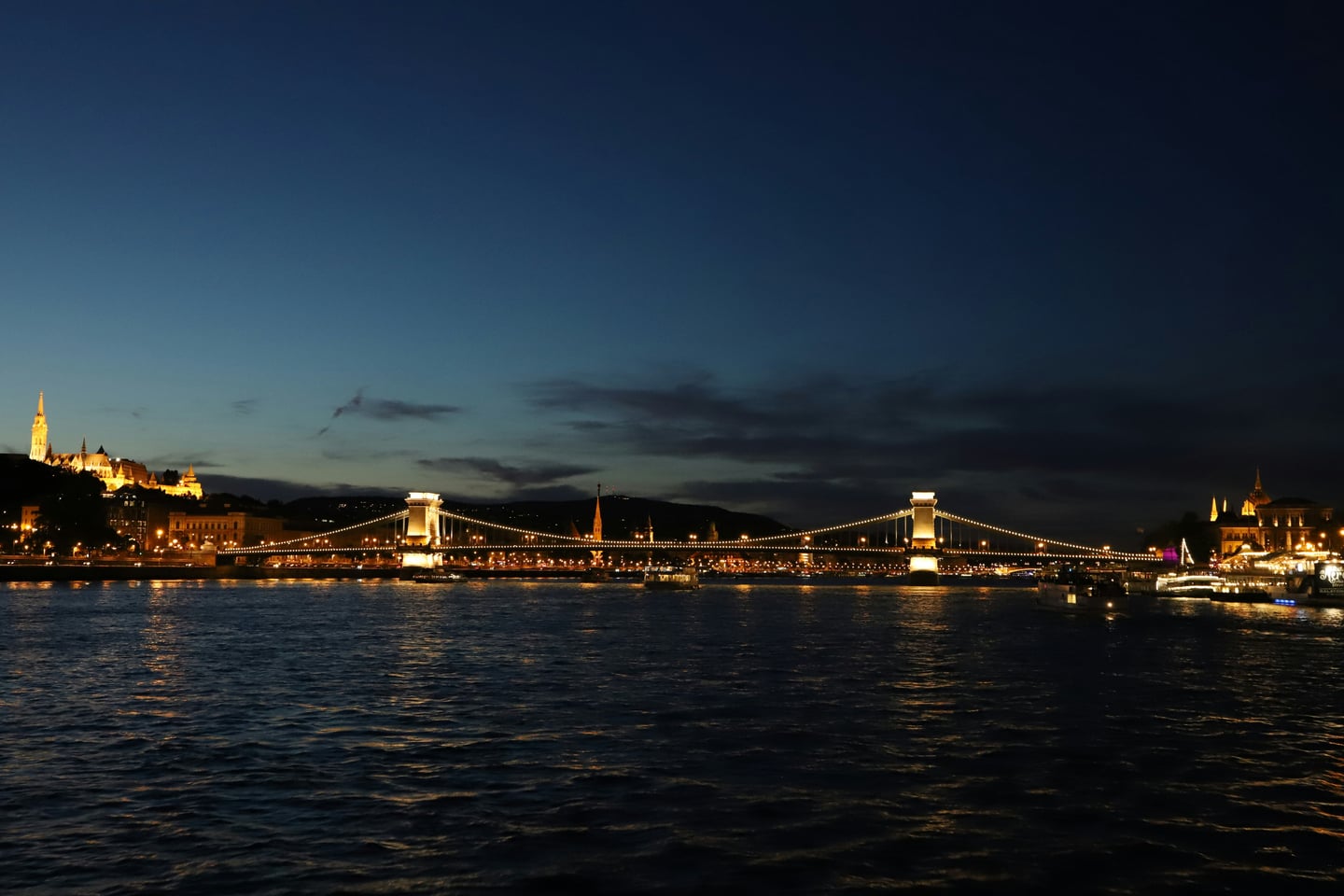 부다페스트 세체니 다리, 어스름한 밤하늘 아래 다뉴브 강을 가로지르며 화려한 황금빛 조명을 밝히고 있는 웅장한 현수교의 야경입니다.