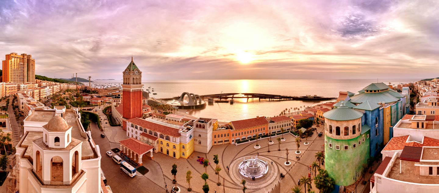 푸꾸옥 선셋타운, 황금빛 노을이 내리는 해안가를 따라 펼쳐진 이국적인 유럽풍 건물들과 높은 시계탑의 파노라마 전경입니다.
