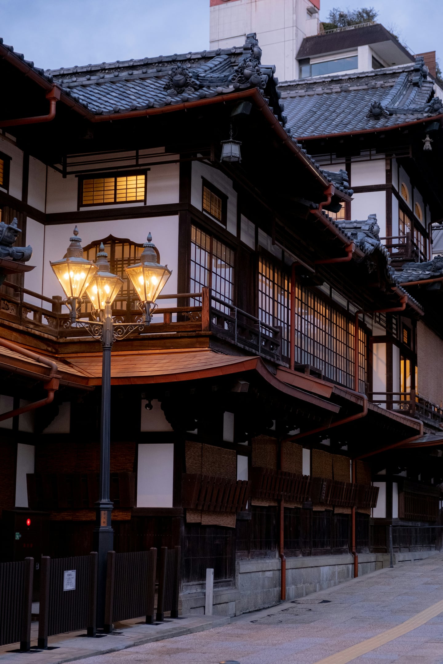 마쓰야마 도고 온천, 해 질 녘 은은한 가로등 불빛 아래 고풍스러운 목조 온천 건물의 전통적인 미가 돋보이는 풍경입니다.