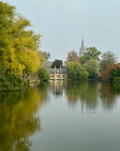 브뤼헤 사랑의 호수, 잔잔한 수면 위로 비치는 고풍스러운 건축물과 가을빛으로 물든 나무들이 어우러진 낭만적인 풍경입니다.