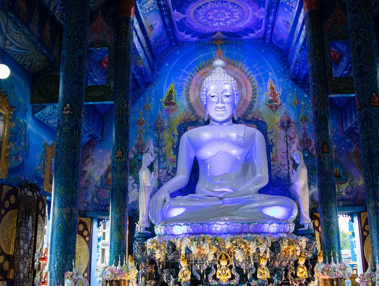 치앙라이 블루 사원, 화려한 푸른색 벽화로 둘러싸인 신비로운 분위기 속 거대한 흰색 불상이 안치된 내부 전경입니다.