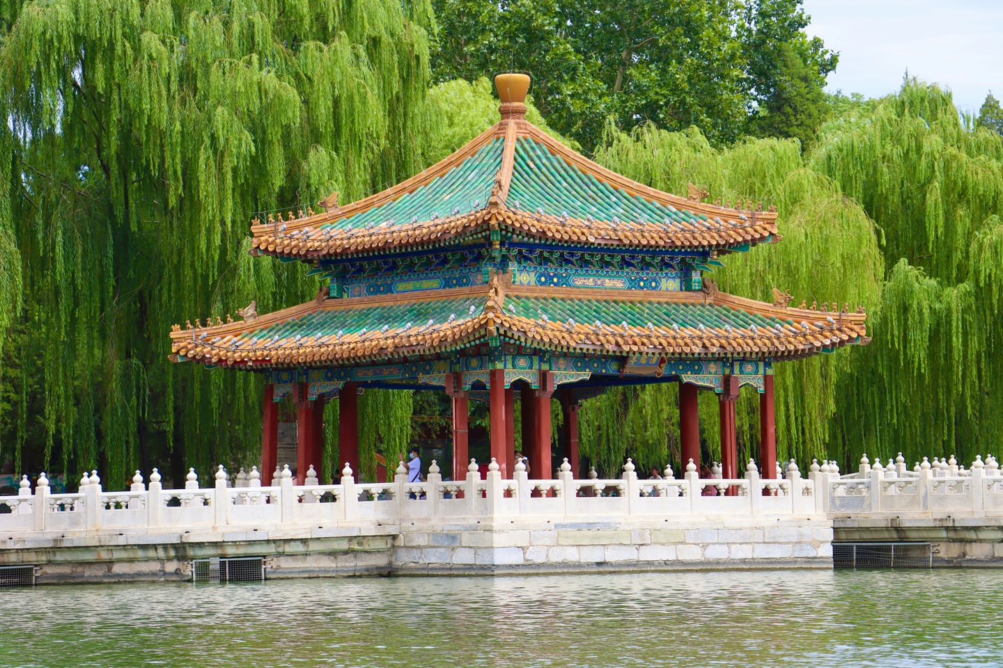 베이징 북해공원, 호수 위 화려한 청록색 기와지붕을 얹은 전통 정자와 푸른 버드나무가 어우러진 평화로운 풍경입니다.