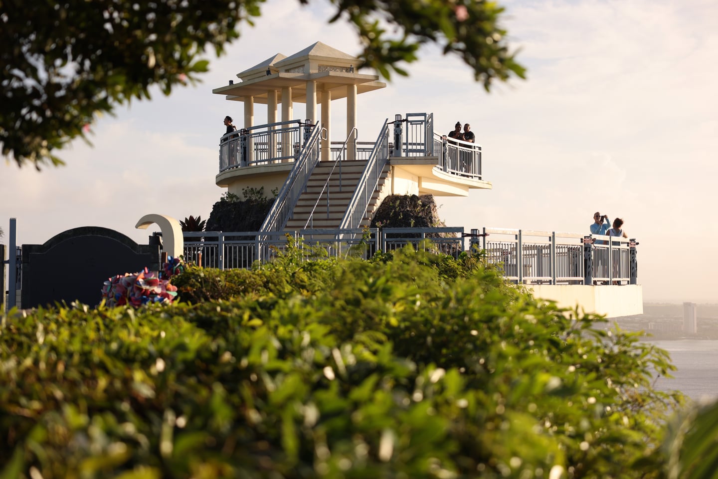 괌 사랑의 절벽, 푸른 숲 위로 솟아오른 2층 전망대에서 탁 트인 바다 경치를 감상하는 관광객들의 모습입니다.