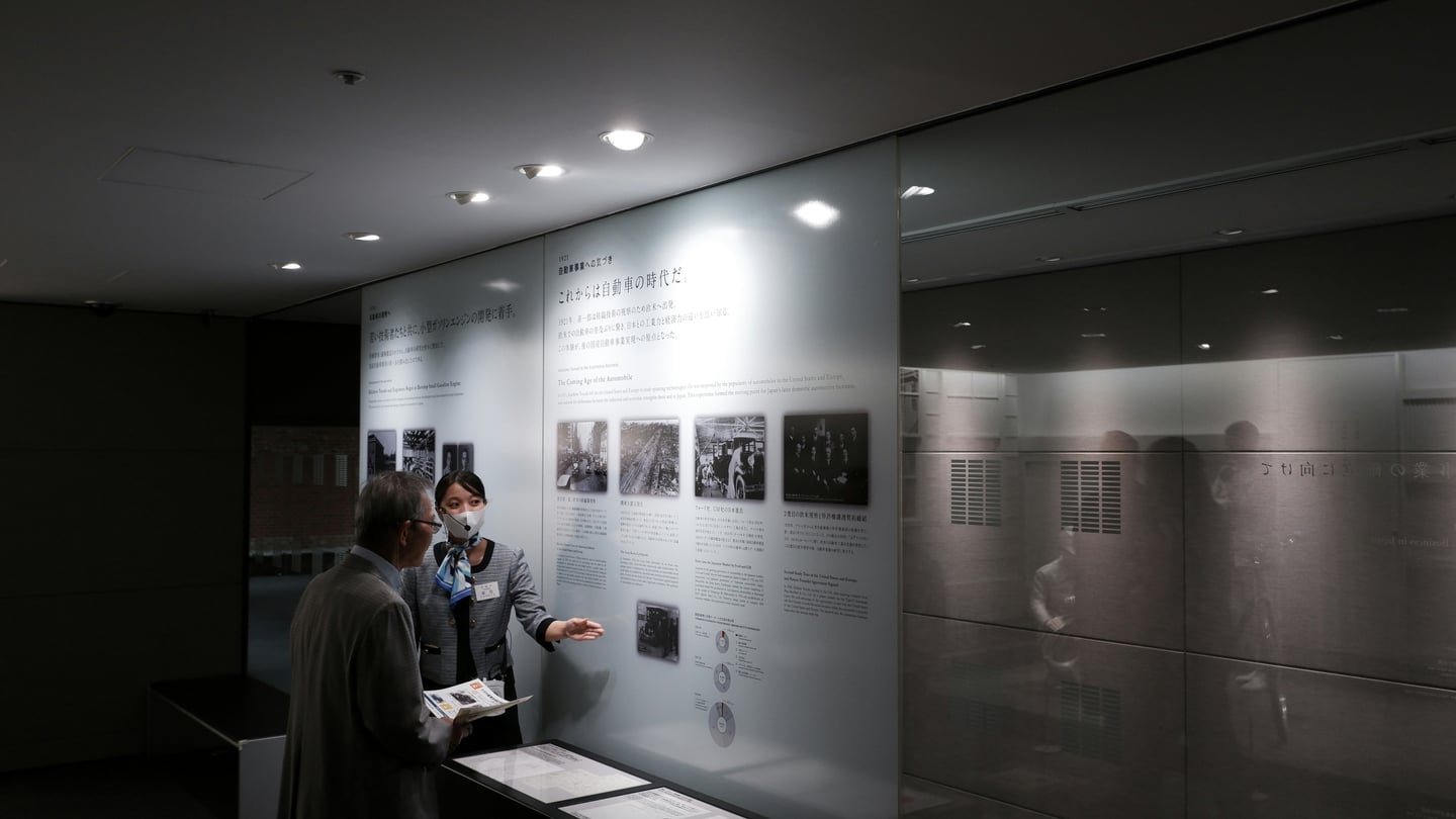 나고야 도요타 산업 기술 기념관, 박물관 직원이 관람객에게 도요타의 자동차 역사 전시물을 설명하는 모습.