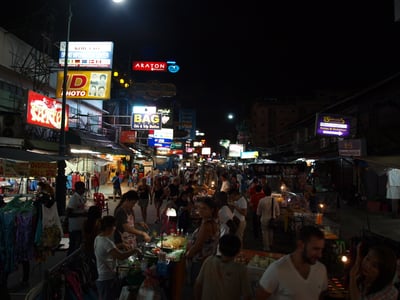 방콕 카오산 로드, 화려한 네온사인 아래 북적이는 인파와 다양한 길거리 음식을 즐기는 관광객들로 가득한 밤거리 풍경입니다.