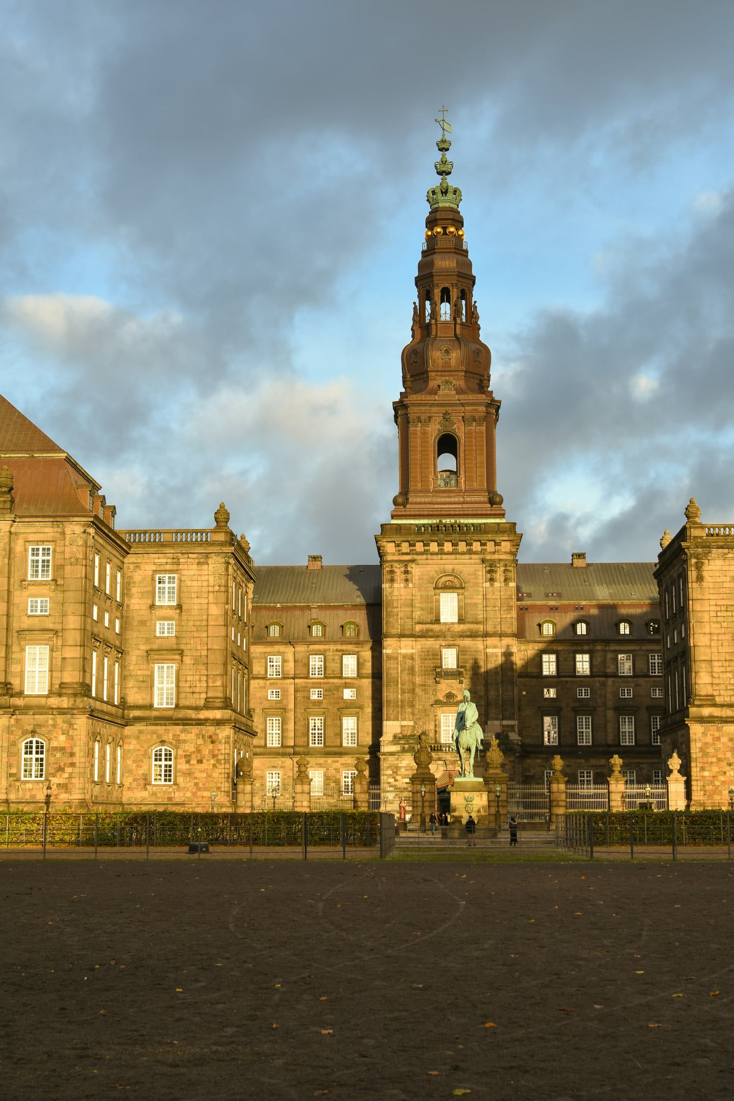 코펜하겐 크리스티안보르 궁전, 노을빛을 받아 황금빛으로 빛나는 웅장한 궁전의 첨탑과 기마상이 있는 풍경입니다.