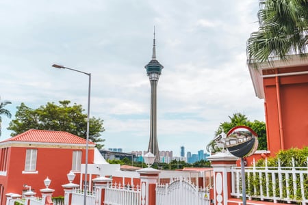 마카오 마카오 타워, 붉은색 건물과 흰색 울타리 사이로 보이는 높고 웅장한 타워의 전경이 인상적입니다.