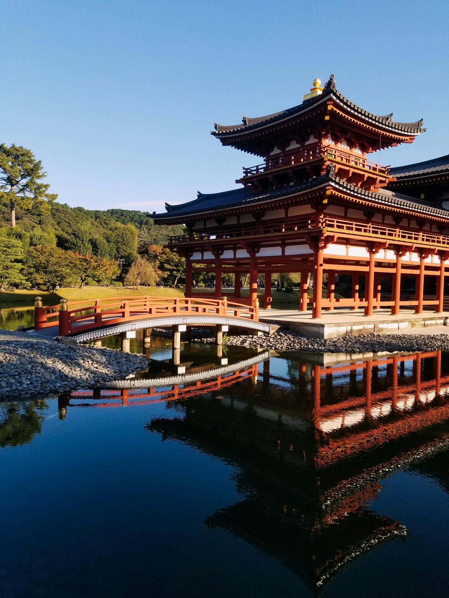 교토 뵤도인, 맑은 연못 위에 붉은 봉황당 건물과 아치형 목조 다리가 선명하게 투영된 평화로운 풍경입니다.