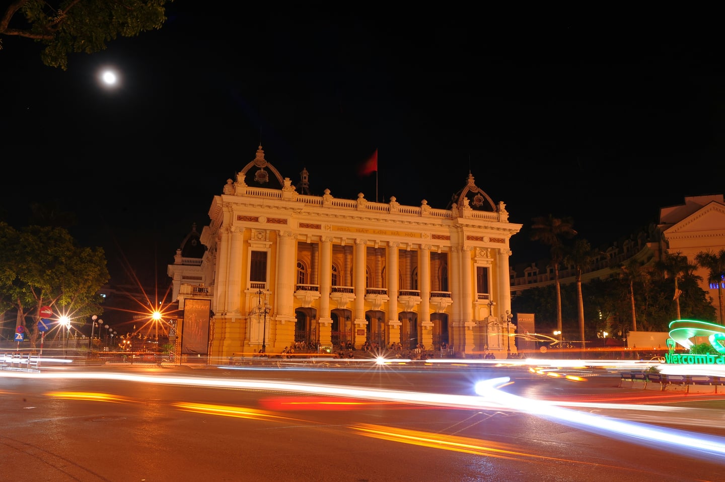 하노이 하노이 오페라 하우스, 화려한 야간 조명과 도로 위를 지나는 차량들의 역동적인 빛의 궤적이 어우러진 신고전주의 건축물의 전경입니다.