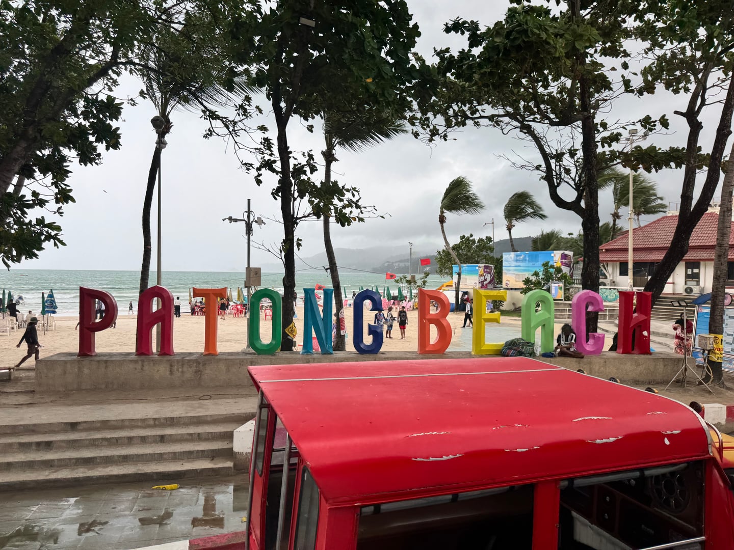 푸켓 파통 비치, 해변 입구에 세워진 화려한 무지개색 대형 영문 이름 조형물과 야자수가 어우러진 활기찬 해안가 풍경입니다.