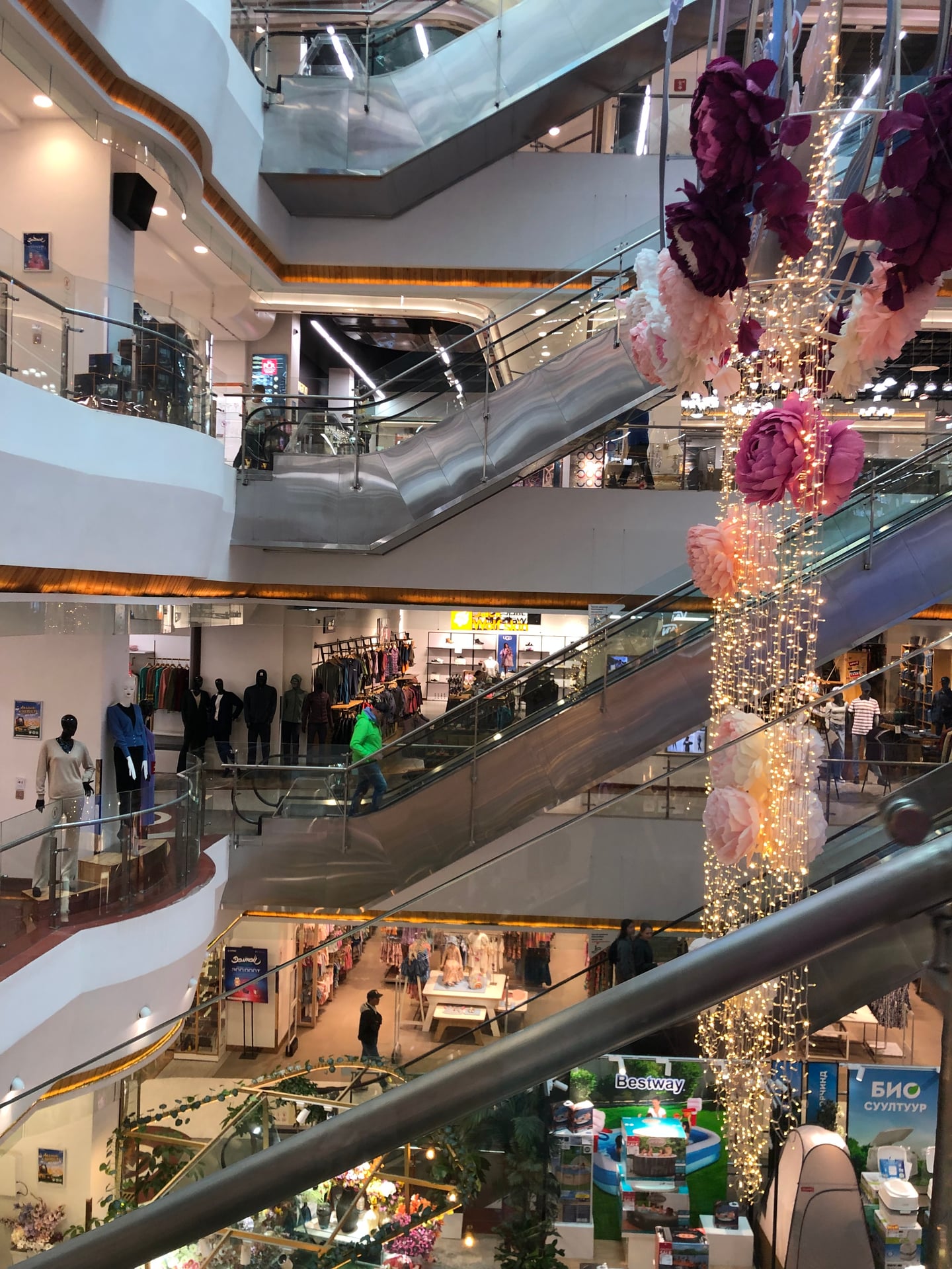울란바토르 국영 백화점, 화려한 꽃 장식과 조명이 어우러진 현대적인 에스컬레이터와 쇼핑몰 내부의 세련된 전경입니다.