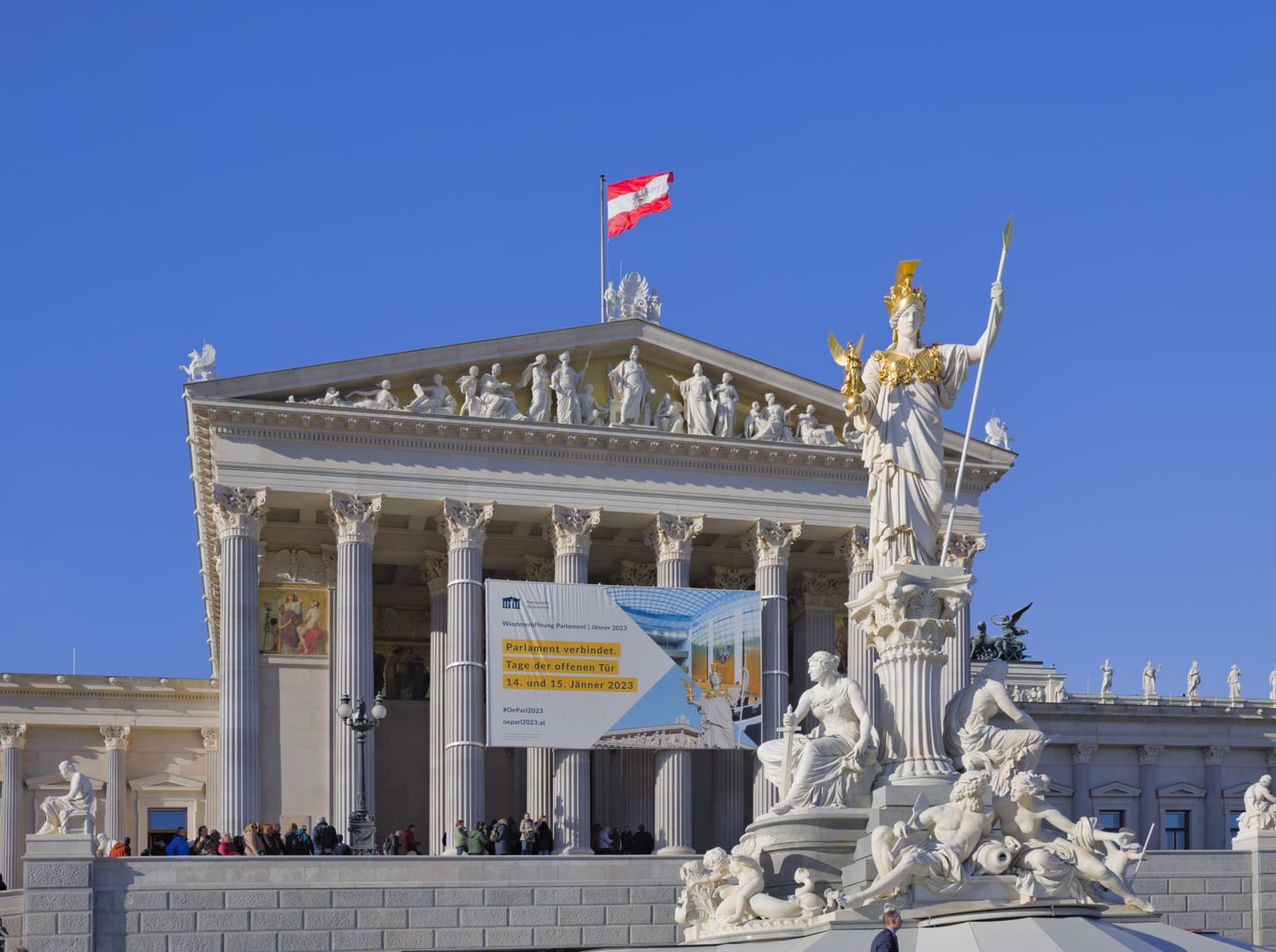 빈 국회의사당, 푸른 하늘 아래 웅장한 그리스식 기둥과 황금빛 아테나 여신상이 조화를 이루는 오스트리아의 역사적 건축물입니다.