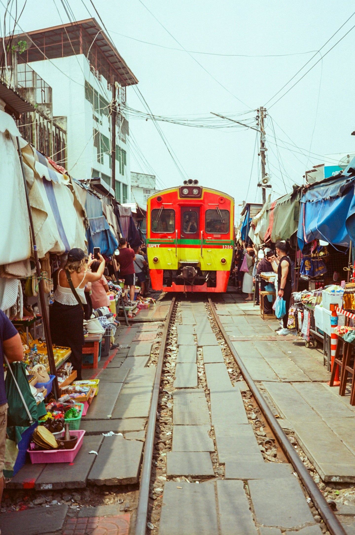 방콕 매끌렁 기찻길 시장, 좁은 시장 골목 사이로 화려한 색상의 기차가 들어오고 상인들과 관광객들이 선로 양옆으로 비켜선 이색적인 풍경입니다.